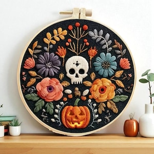 May include: A circular black fabric embroidery hoop with a skull and floral design. The embroidery features a pumpkin, flowers in orange, purple, and blue, and leaves. The hoop is made of wood.