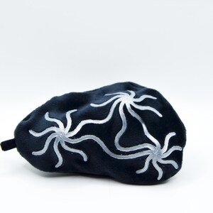 K&ouml;nnte beinhalten: Eine dunkelblaue Schlafmaske mit drei wei&szlig;en, stilisierten Blumenmustern. Die Maske besteht aus einem weichen, pl&uuml;schigen Material und hat eine kleine, schwarze Lasche. Das Design ist schlicht und elegant, f&uuml;r Entspannung und Schlaf.