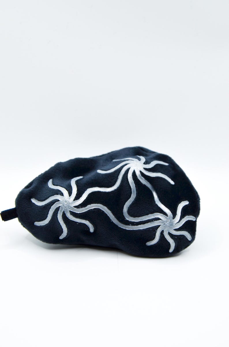 K&ouml;nnte beinhalten: Eine dunkelblaue Schlafmaske mit drei wei&szlig;en, stilisierten Blumenmustern. Die Maske besteht aus einem weichen, pl&uuml;schigen Material und hat eine kleine, schwarze Lasche. Das Design ist schlicht und elegant, f&uuml;r Entspannung und Schlaf.