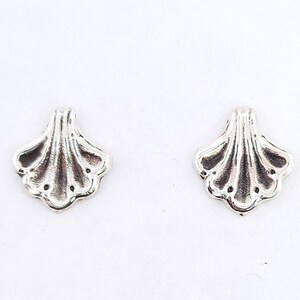 Puede incluir: Un par de pendientes de plata con diseño de concha de vieira.