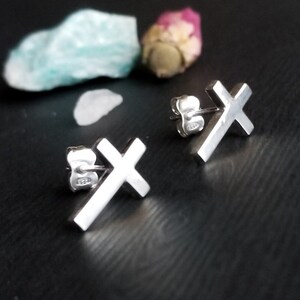 May include: A pair of silver cross stud earrings. The earrings are small and simple, with a minimalist design.