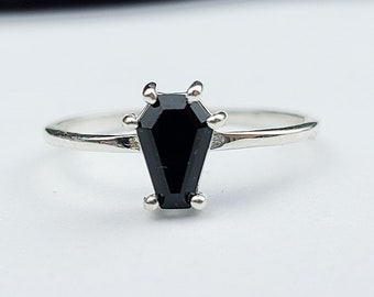 May include: A silver ring with a black coffin-shaped gemstone. The ring is on a white background.