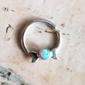May include: A silver hoop earring with a crescent moon design and a small opal gemstone in the center.