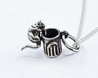 May include: A silver necklace with a charm of a cat climbing into a trash can.