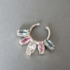 Puede incluir: Un aro de nariz de plata con un grupo de piedras preciosas de forma ovalada. Las piedras preciosas son en tonos de azul, rosa y blanco.