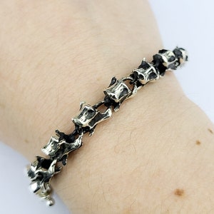 May include: A silver bracelet with a unique design featuring a series of connected bone-shaped links.
