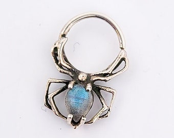 May include: Silver hoop earring with a spider design and a blue gemstone in the center.