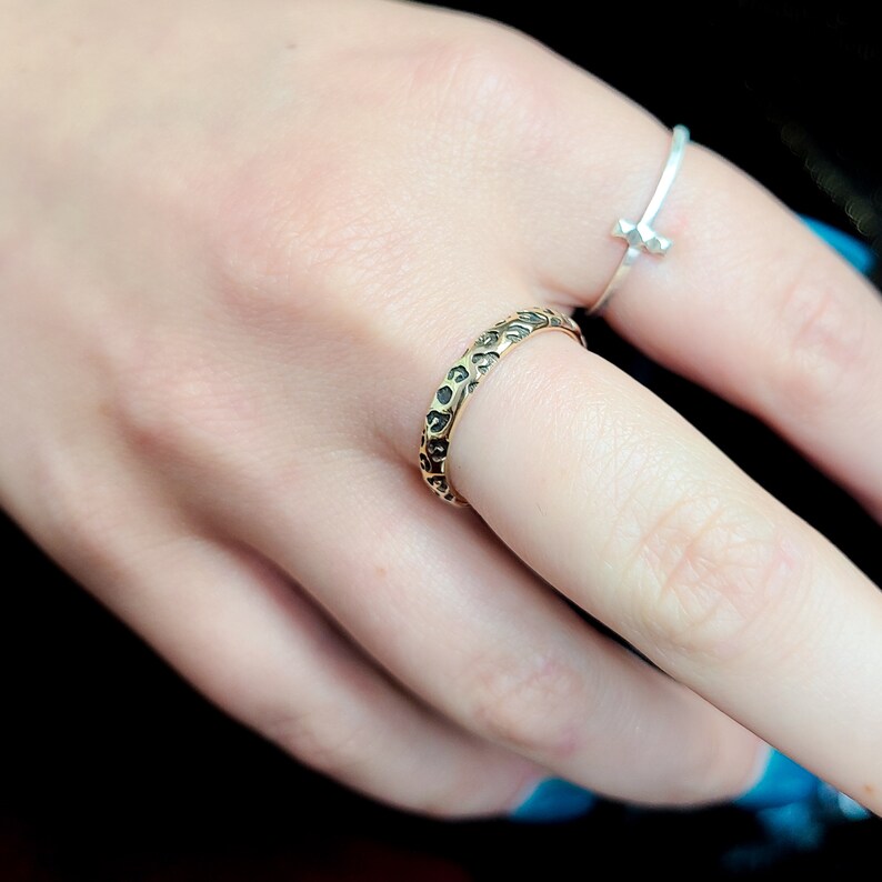 May include: A gold ring with a textured surface featuring a leopard print design. The ring is worn on a finger.