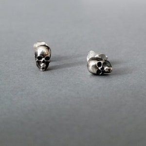 May include: A pair of silver skull stud earrings. The earrings are small and detailed, with a realistic skull design.