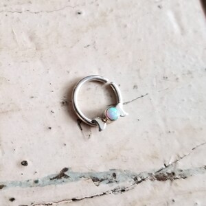 May include: Silver hoop earring with a crescent moon design and a small opal gemstone.