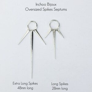 May include: Two silver septum rings with spikes. The ring on the left has extra long spikes that are 48mm long. The ring on the right has long spikes that are 28mm long.