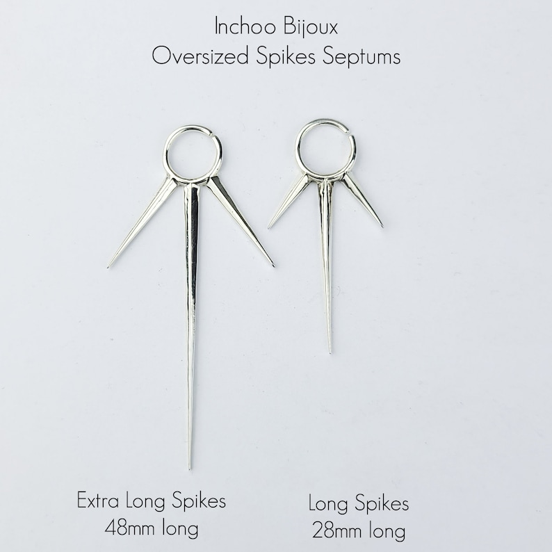 May include: Two silver septum rings with spikes. The ring on the left has extra long spikes that are 48mm long. The ring on the right has long spikes that are 28mm long.