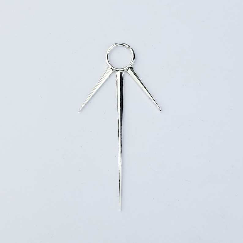 May include: Silver body jewelry with a circular hoop and three sharp points extending from the hoop.