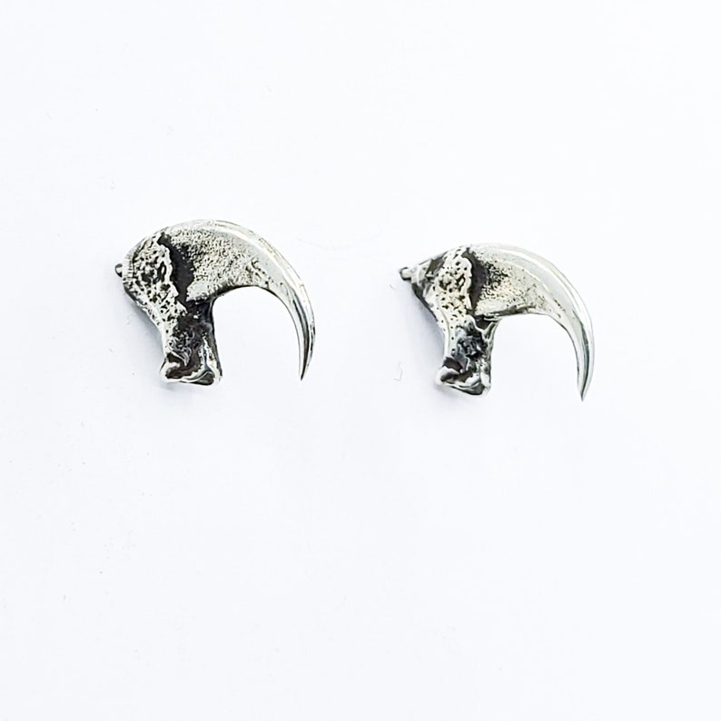 May include: A pair of silver earrings shaped like claws. The earrings are detailed and have a textured finish.