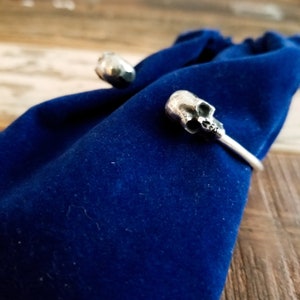 May include: A silver skull cuff bracelet with a detailed skull design. The bracelet is on a blue velvet background.