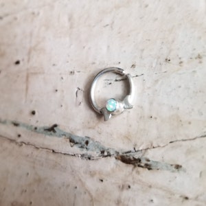 May include: A silver hoop earring with a crescent moon design and a small opal gemstone.