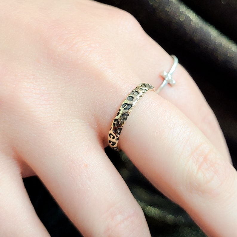 May include: A gold ring with a textured leopard print design. The ring is worn on a finger.