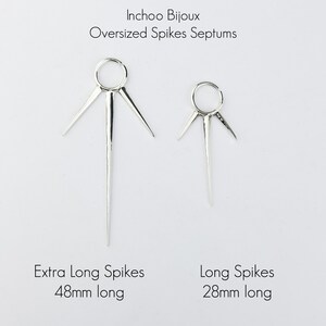 May include: Two silver septum rings with long, pointed spikes. The ring on the left has spikes that are 48mm long, and the ring on the right has spikes that are 28mm long.  Inchoo Bijoux Oversized Spikes Septums. Extra Long Spikes 48mm long. Long Spikes 28mm long.