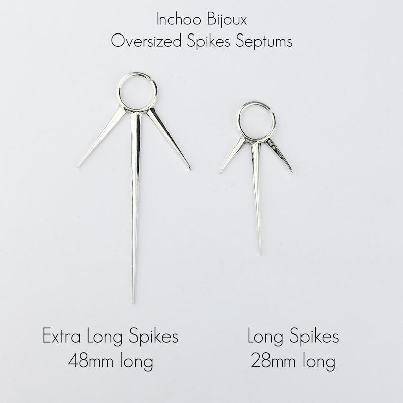 May include: Two silver septum rings with long, pointed spikes. The ring on the left has spikes that are 48mm long, and the ring on the right has spikes that are 28mm long.  Inchoo Bijoux Oversized Spikes Septums. Extra Long Spikes 48mm long. Long Spikes 28mm long.