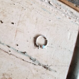 May include: A silver hoop earring with a crescent moon design and a small opal gemstone in the center.