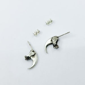 May include: A pair of silver claw earrings. Each earring features a detailed claw design with a textured surface. The earrings are attached to a silver post with a butterfly backing.