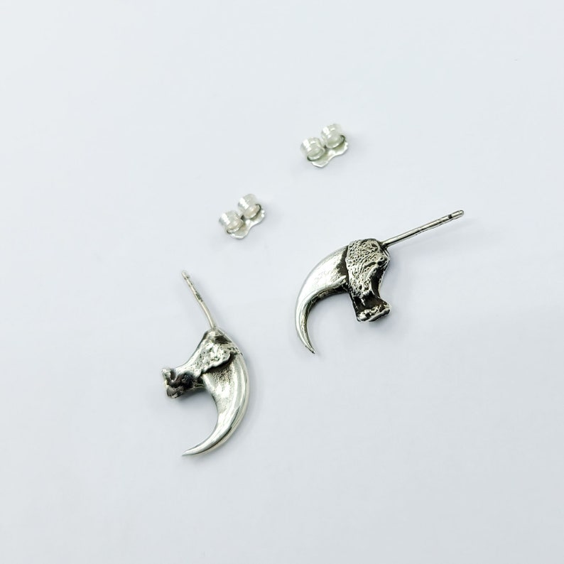 May include: A pair of silver claw earrings. Each earring features a detailed claw design with a textured surface. The earrings are attached to a silver post with a butterfly backing.