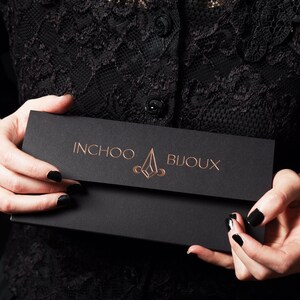 May include: A black envelope with the text "INCHOO BIJOUX" in gold lettering. The envelope has a geometric design in gold.