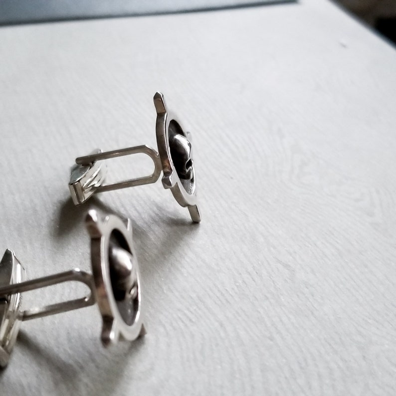 May include: A pair of silver cufflinks with a circular design. The cufflinks have a textured surface and a raised design in the center.