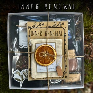 May include: A clear box with a tea-themed gift set, tied with twine. The box contains tea bags, a dried orange slice, and a card that reads "Inner Renewal". The text "Tea Box with Gift Wrapping" is at the bottom.