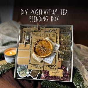 May include: A DIY Postpartum Tea Blending Box containing tea ingredients, such as rose petals and herbs, and a tea infuser. The box is tied with twine and decorated with a dried orange slice. The text "Mothers Tea Kit" is visible.