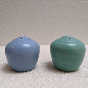 Peut inclure: Deux salières et poivrières en céramique. L'une est bleu clair, l'autre turquoise. Chaque salière a trois trous sur le dessus. Les salières ont une forme arrondie et bulbeuse, pour la cuisine.
