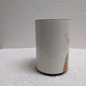 Puede incluir: Taza de cer&aacute;mica blanca con borde rojo y base negra. La taza presenta un dise&ntilde;o floral con flores rosas y hojas verdes. La taza es cil&iacute;ndrica y se apoya sobre una superficie blanca.