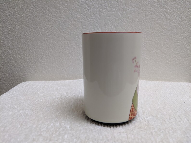 Puede incluir: Taza de cer&aacute;mica blanca con borde rojo y base negra. La taza presenta un dise&ntilde;o floral con flores rosas y hojas verdes. La taza es cil&iacute;ndrica y se apoya sobre una superficie blanca.