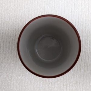 Puede incluir: Una taza de cer&aacute;mica con interior gris y borde marr&oacute;n oscuro. La taza est&aacute; vac&iacute;a y se encuentra sobre una superficie blanca y texturizada. La imagen est&aacute; tomada desde arriba.