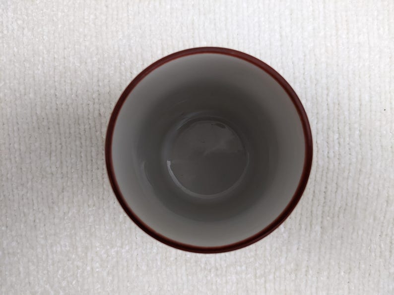 Puede incluir: Una taza de cer&aacute;mica con interior gris y borde marr&oacute;n oscuro. La taza est&aacute; vac&iacute;a y se encuentra sobre una superficie blanca y texturizada. La imagen est&aacute; tomada desde arriba.