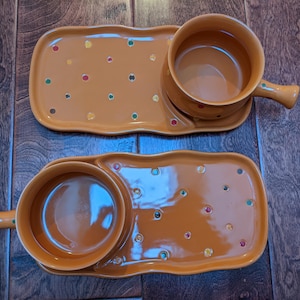 May include: Two orange ceramic soup and cracker sets. Each set includes a rectangular tray with a circular indentation for a soup bowl and a handle. The trays are decorated with colorful polka dots.