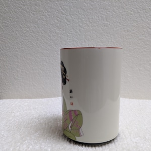 Puede incluir: Taza de cer&aacute;mica blanca con borde rojo, con un dise&ntilde;o de geisha japonesa. La geisha est&aacute; representada con vestimenta tradicional, peinado detallado y kimono colorido. La taza es cil&iacute;ndrica.