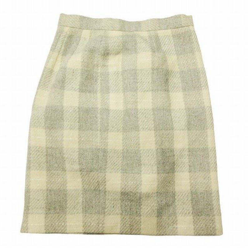 May include: A knee-length skirt with a plaid pattern in shades of cream and gray. The fabric appears to be a woven material, possibly wool or a wool blend. The skirt has a simple, classic design.
