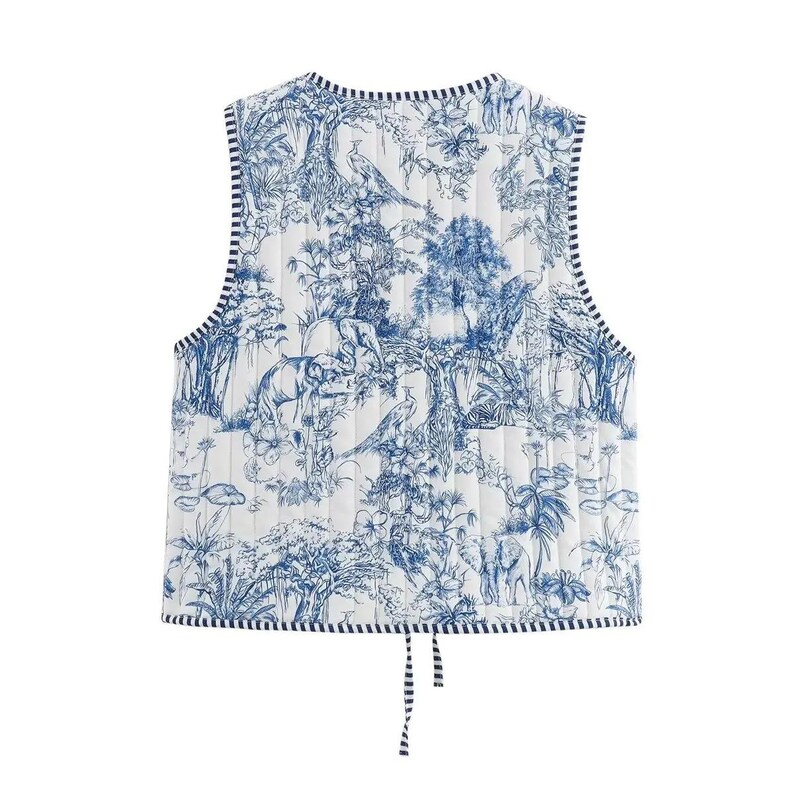 May include: A white quilted vest with a blue toile print featuring a jungle scene with elephants, birds, and foliage. The vest has a navy blue and white striped trim and ties at the waist.