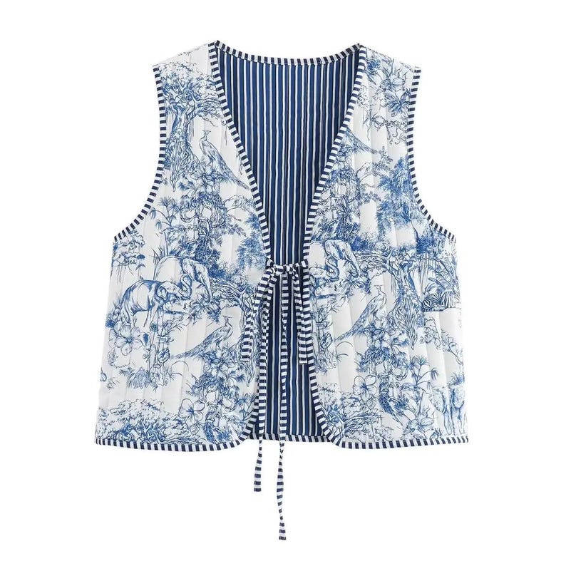 May include: Reversible quilted vest featuring a blue and white toile print with elephants, birds, and floral elements. The vest has a striped blue interior and a tie closure. The vest is sleeveless and has a V-neck.