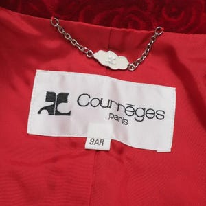 May include: Close-up of a red jacket lining with a white label featuring the brand name "Courr&egrave;ges paris" in black text. A silver chain is attached to a white cloud-shaped tag. The lining is a solid red color.