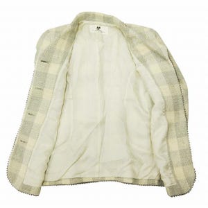 May include: A light-colored, open blazer with a checkered pattern in shades of cream and gray. The blazer has a notched collar, three buttons, and a decorative trim along the edges. The interior lining is a solid cream color.