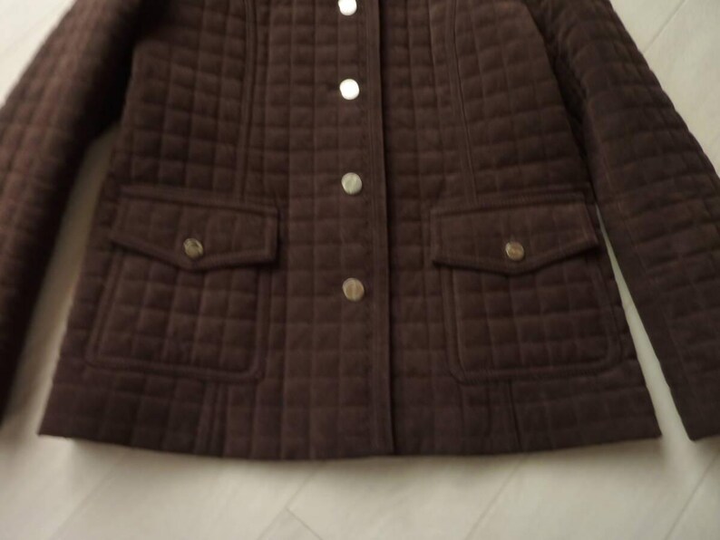May include: A brown quilted jacket with a button-up front and two front pockets. The jacket has a diamond pattern and gold-colored buttons. The sleeves are long and the jacket appears to be made of a soft material.