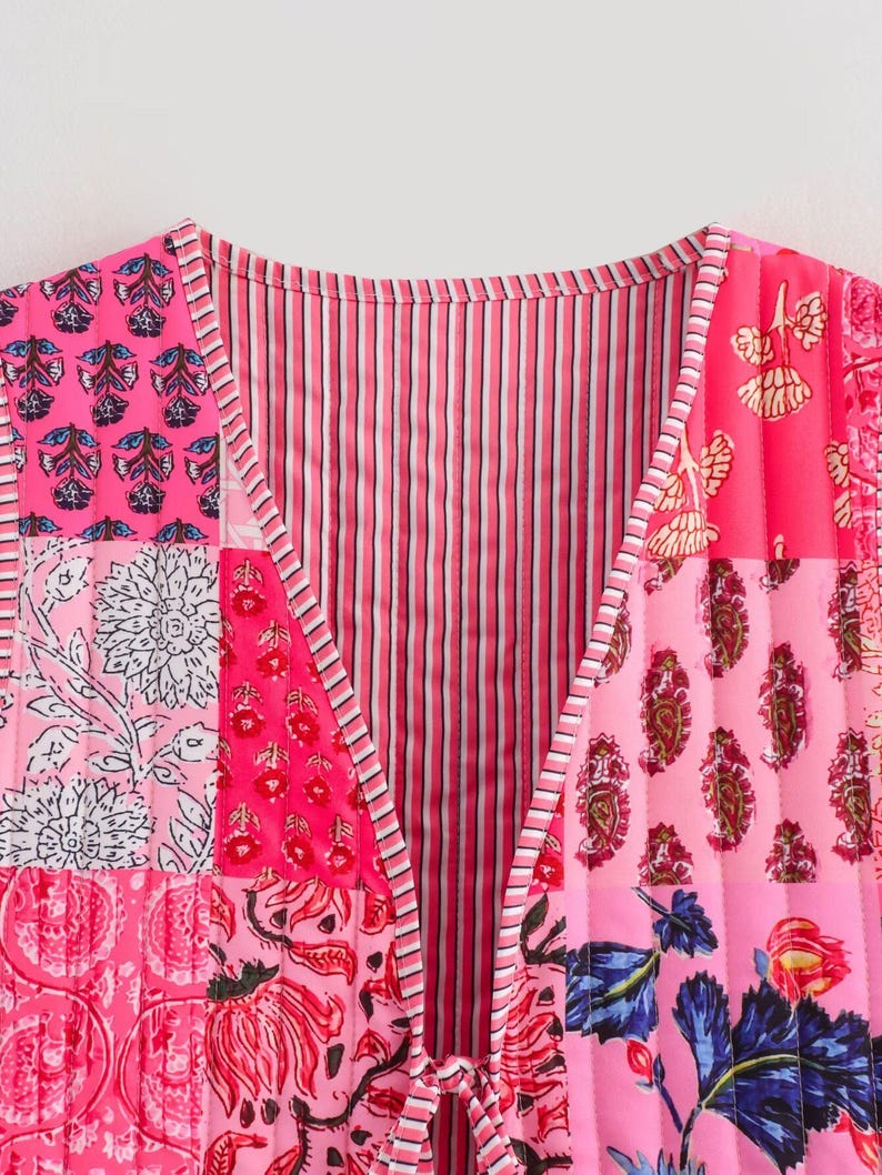 May include: A patchwork vest in shades of pink, featuring floral and paisley patterns. The vest has a V-neck and a tie closure. The design includes vertical stripes and quilted sections, creating a vibrant and textured look.