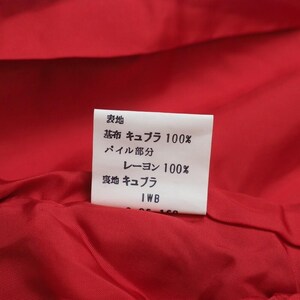 May include: Close-up of a red fabric interior with a white tag. The tag features Japanese text indicating the fabric composition: 100% Cupro for the base fabric, 100% Rayon for the pile, and Cupro for the lining. The tag also includes the letters "IWB".