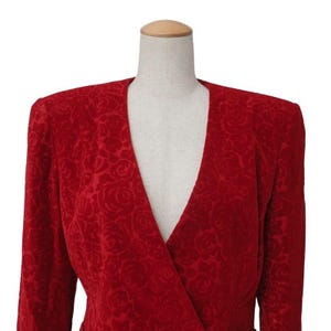 May include: A red blazer with a V-neck design, displayed on a mannequin. The blazer features a rose pattern embossed throughout the fabric. The sleeves are long, and the shoulders are slightly padded.