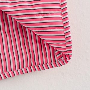 May include: Close-up of a section of fabric with a pink, black, and white striped pattern. The fabric is folded over, revealing the interior lining. The stripes are vertical and evenly spaced, with a stitched seam visible.