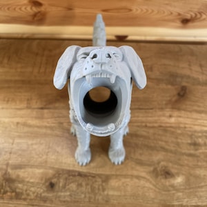 May include: A light grey 3D printed dog figurine with a hollow, open mouth design. The canine figure features visible horizontal layer lines from the printing process, floppy ears, and a textured surface, standing in a forward-facing position.
