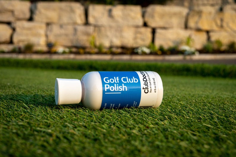 以下が含まれることがあります： 白いスクリューキャップが付いたClubDoctor Golf Club Polishの白いプラスチックボトル。青いラベルには白い文字でGolf Club PolishとClubDoctorと書かれており、ボトルの側面には118mlという容量が印刷されています。