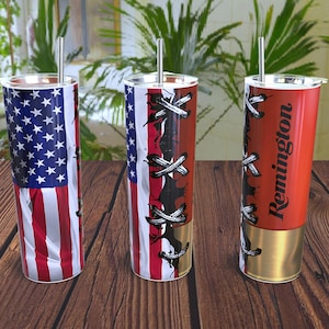 May include: Three stainless steel tumblers with lids and straws. One features the American flag, another has a red, white, and black design, and the third is red with "Remington" printed on it. All three tumblers have a gold-colored base.